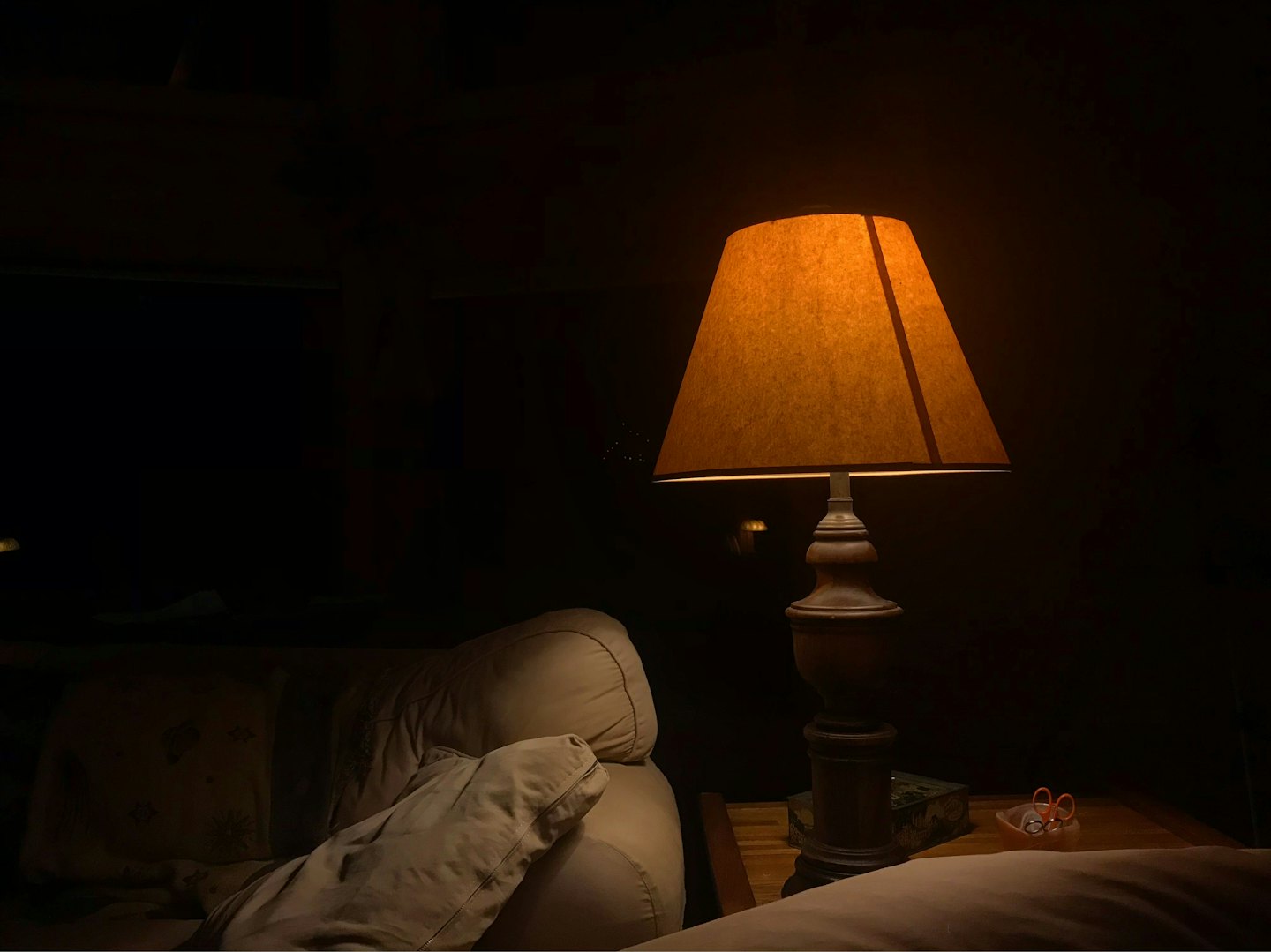 An amber table lamp illuminates a wooden side table and sofa.