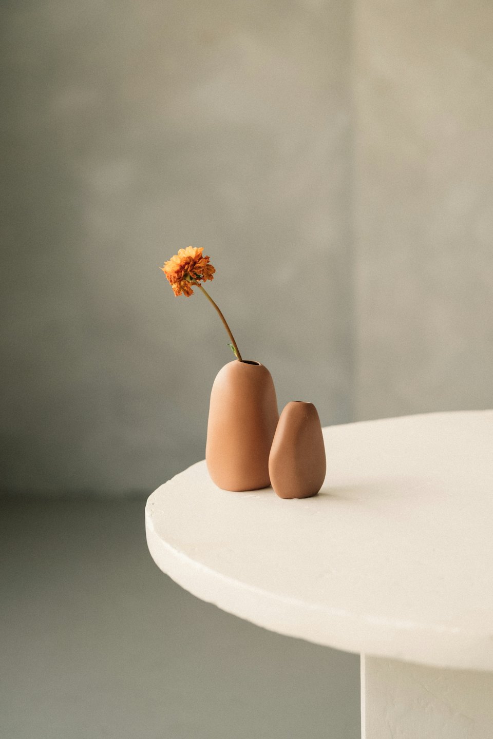 Two terracotta vases with a single flower on a textured table.