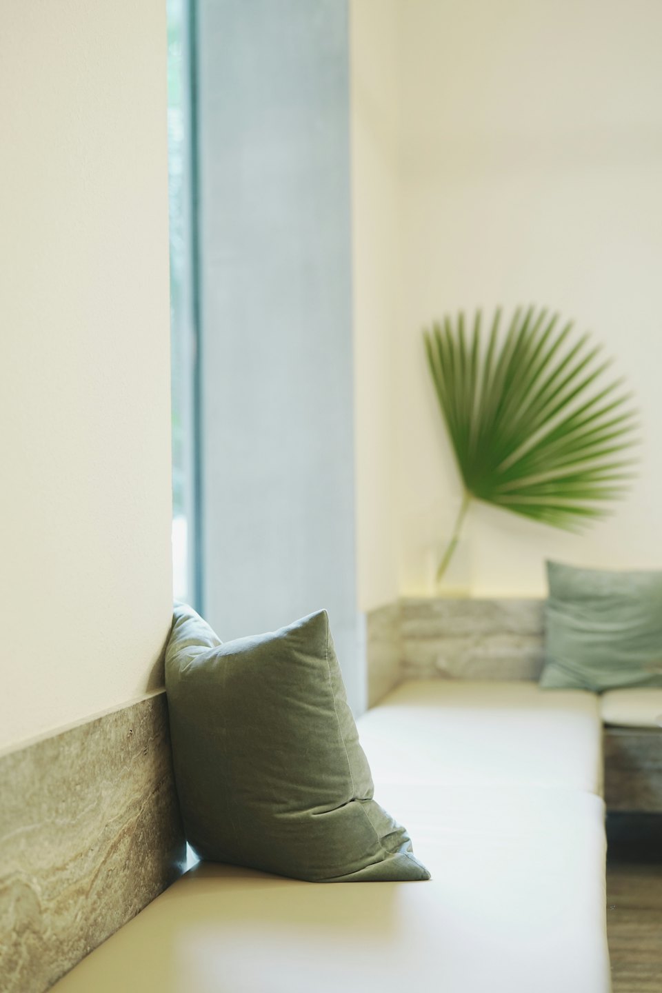 A beige built-in bench with a velvet pillow against a stone wall.