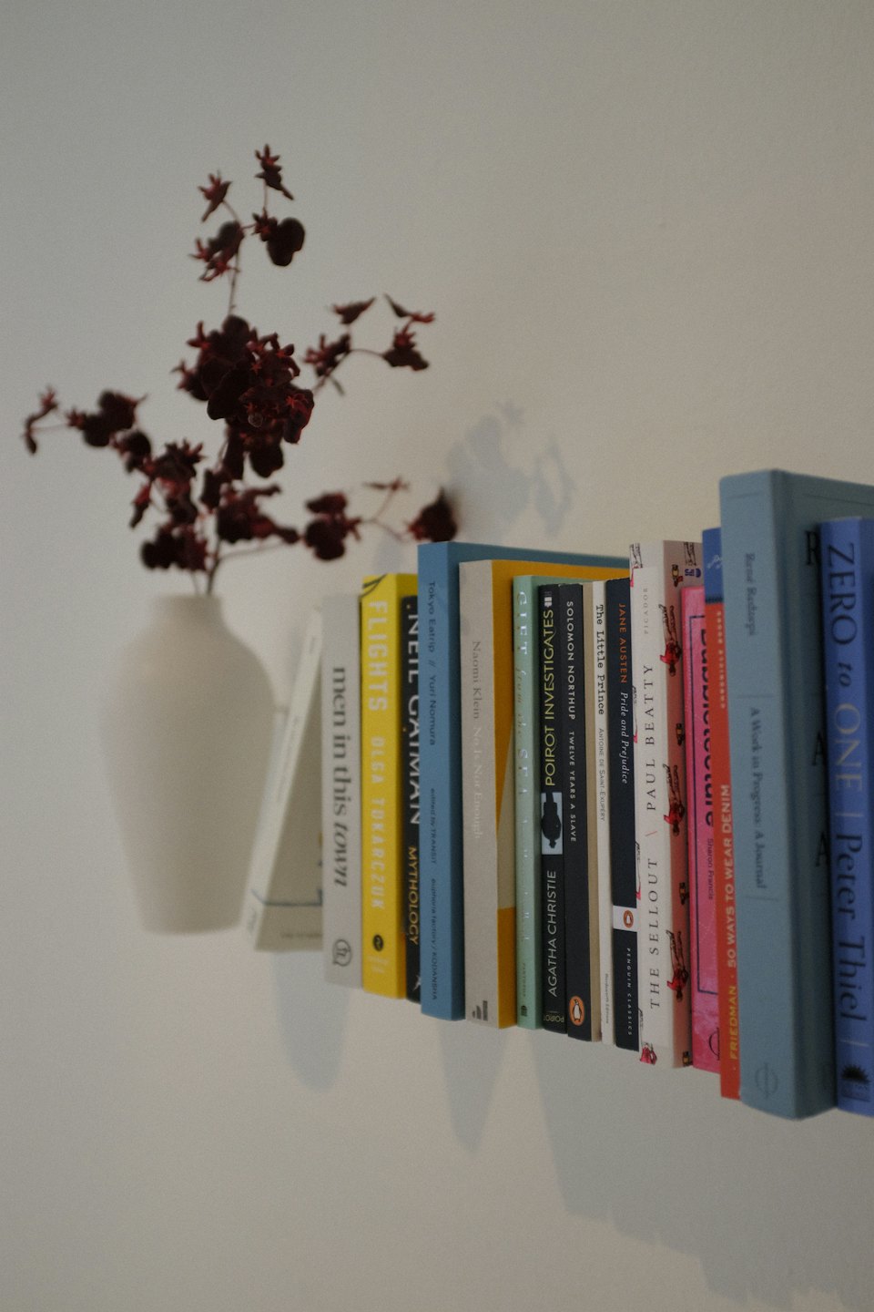 White shelf with colorful books and dried flowers.