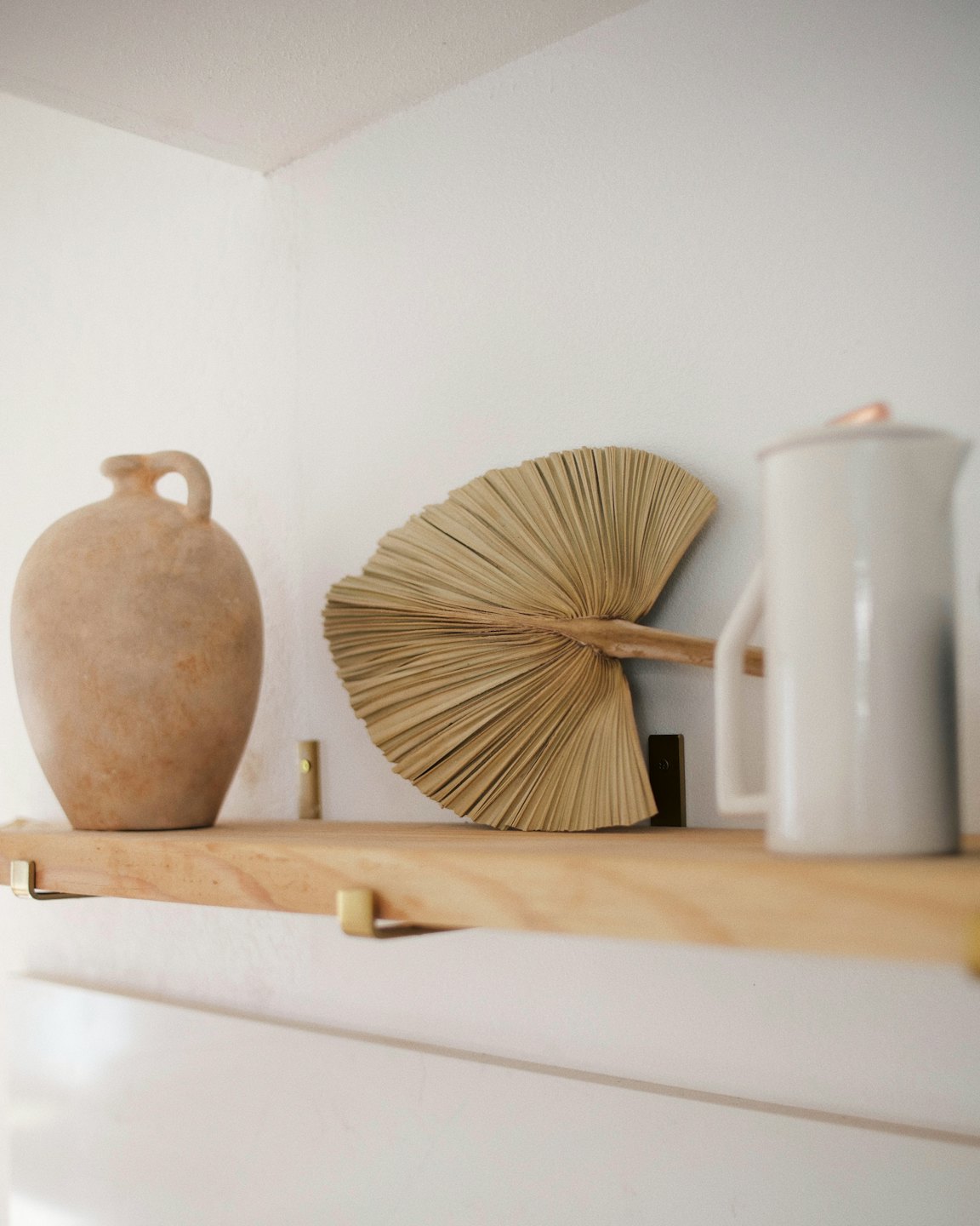 Decorative ceramic jug and pitcher with palm leaf on shelf.