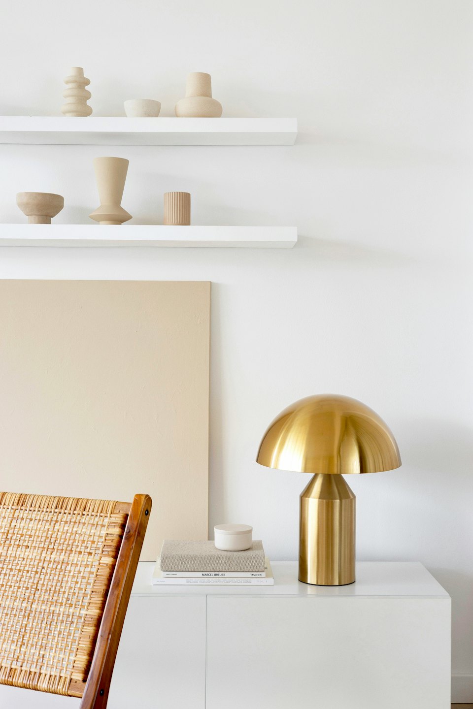 White shelves on a wall display beige vases above a cabinet.