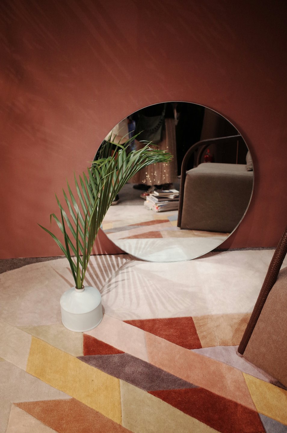 Round mirror leans against terracotta wall with green plant.